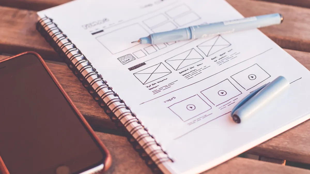 Notebook with website wireframe sketches beside a smartphone on a wooden desk