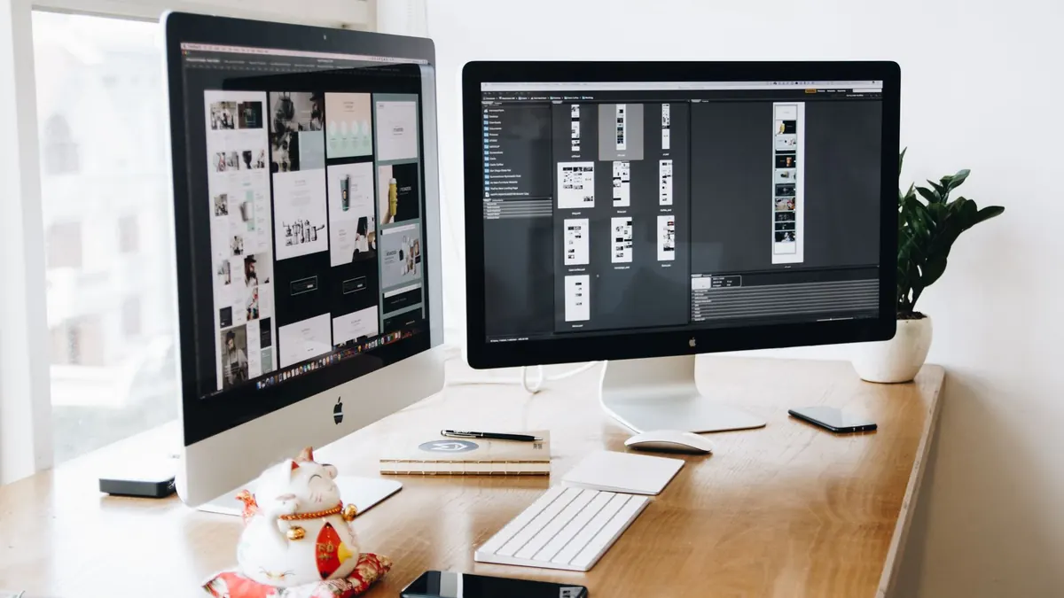 Design workspace with two desktop computers, a keyboard and phones on a desk