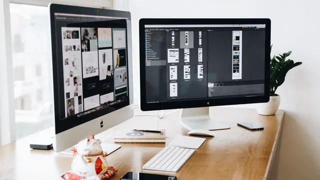 Design workspace with two desktop computers, a keyboard and phones on a desk