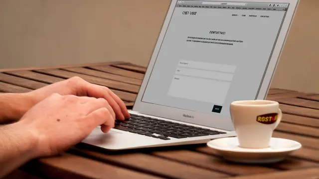 Hands typing on a laptop beside a coffee cup on a wooden table