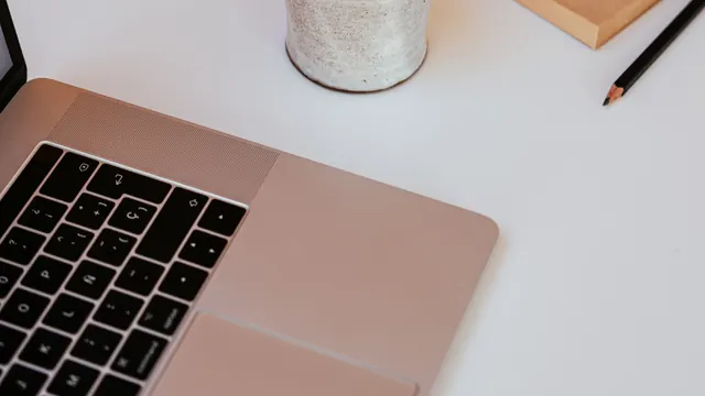 Laptop on a white desk beside a notepad and a pencil