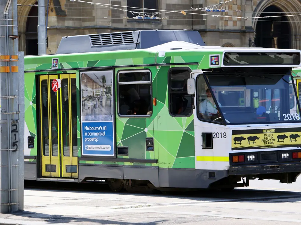 A green and yellow Melbourne tram passing along a city street